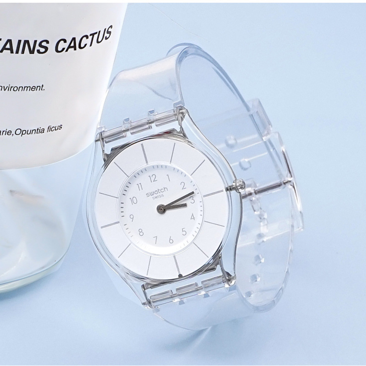 Orologio trasparente con quadrante bianco, cinturino trasparente e la parola 'Swatch'.