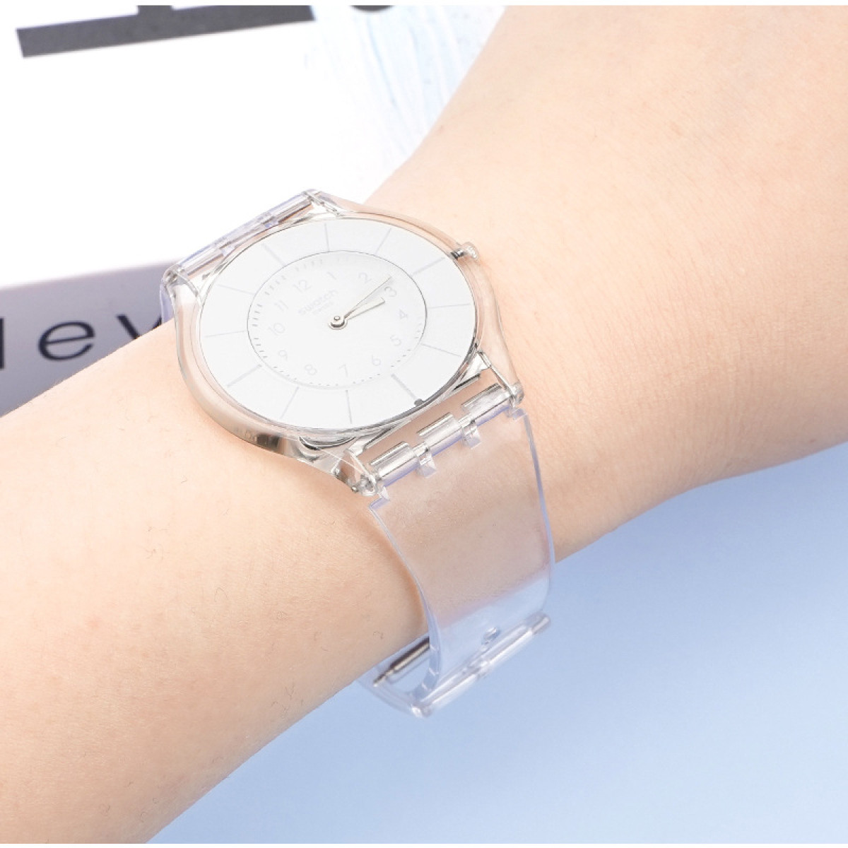 Un orologio trasparente su un polso. L'orologio è trasparente con quadrante bianco e cinturino.