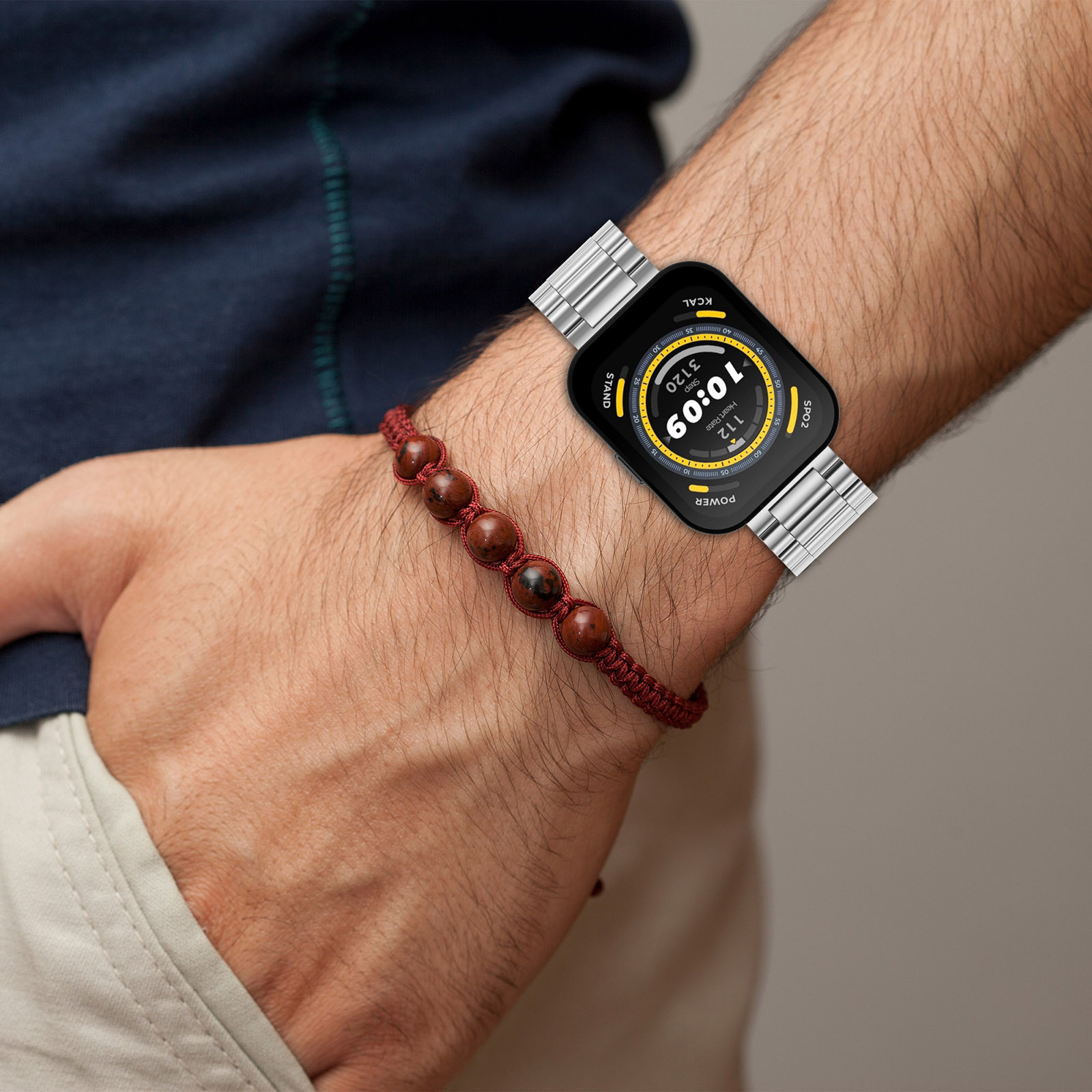 Handgelenk eines Mannes mit Smartwatch, Edelstahlband. Rotes Perlenarmband auch.