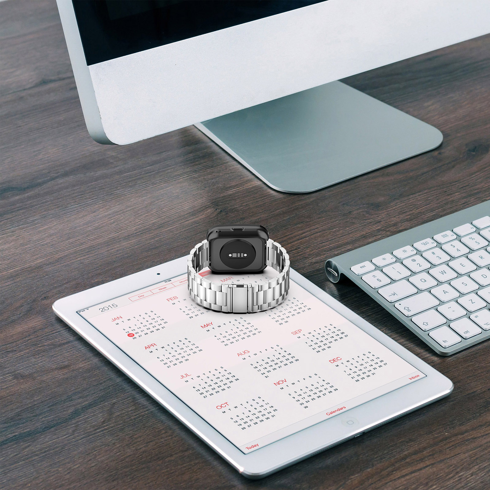 Eine Smartwatch auf einem Kalender und ein Computermonitor im Hintergrund.