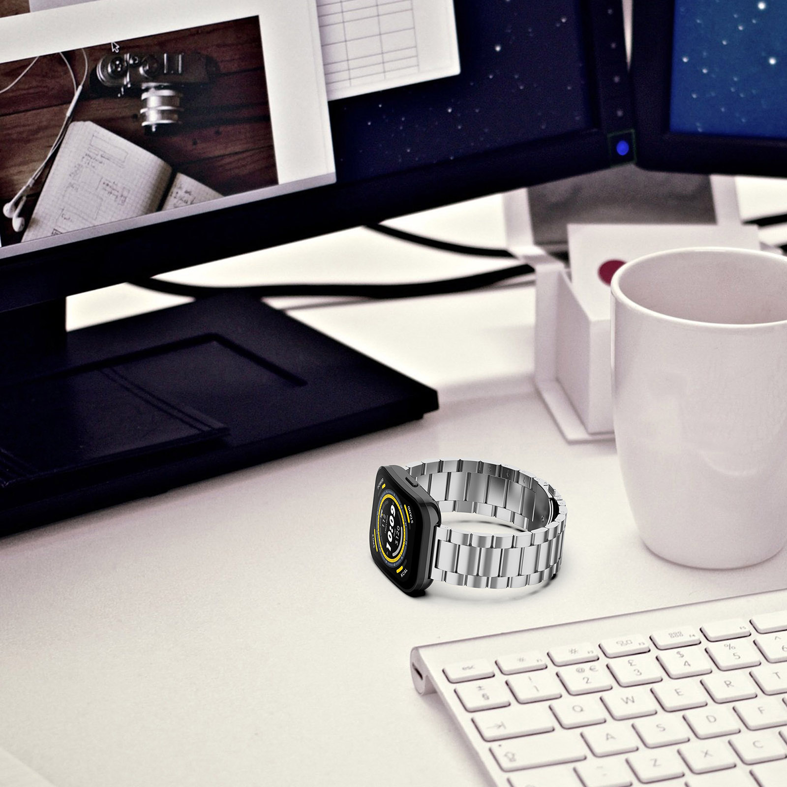 Eine Smartwatch mit silbernem Armband liegt auf einem Schreibtisch. Eine Tastatur und ein Monitor sind im Hintergrund.