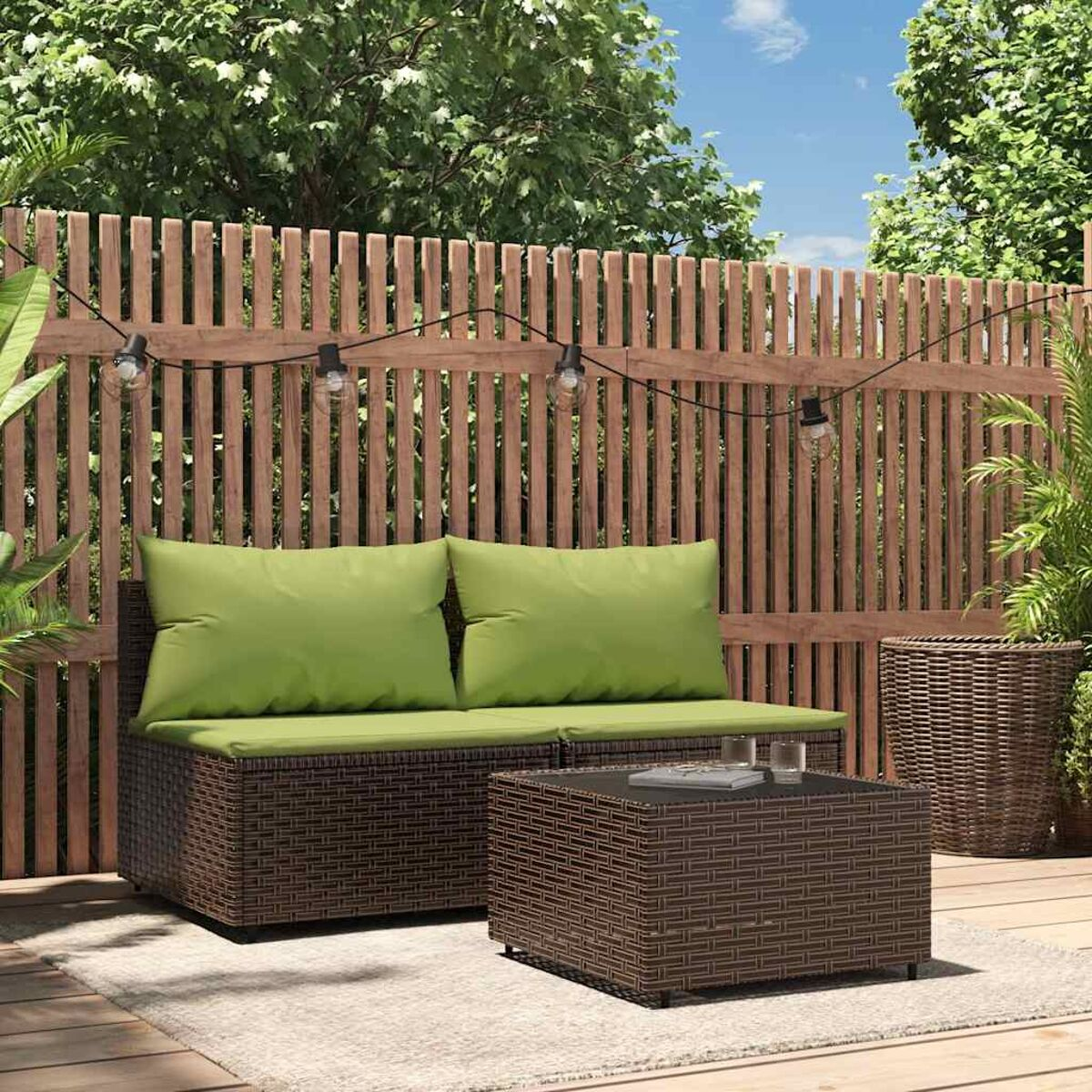 Szene im Freien mit braunem Rattan-Sofa, Tisch und grünen Kissen. Im Hintergrund ist ein Holzzaun.