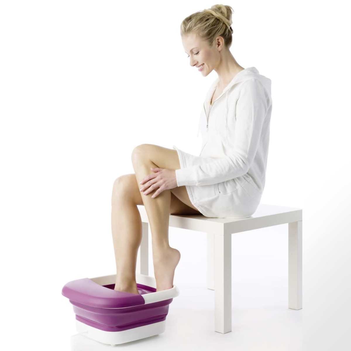 Donna seduta su un tavolo con una spa per i piedi. Un piede è nell'acqua.