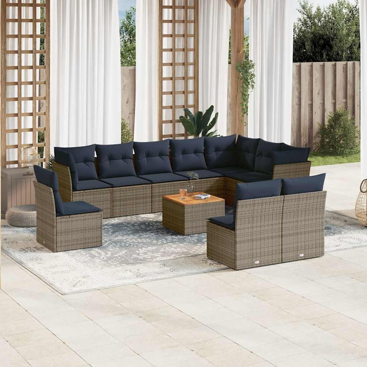 Set patio esterno con cuscini blu scuro. Tavolo in legno. Tende bianche sullo sfondo.