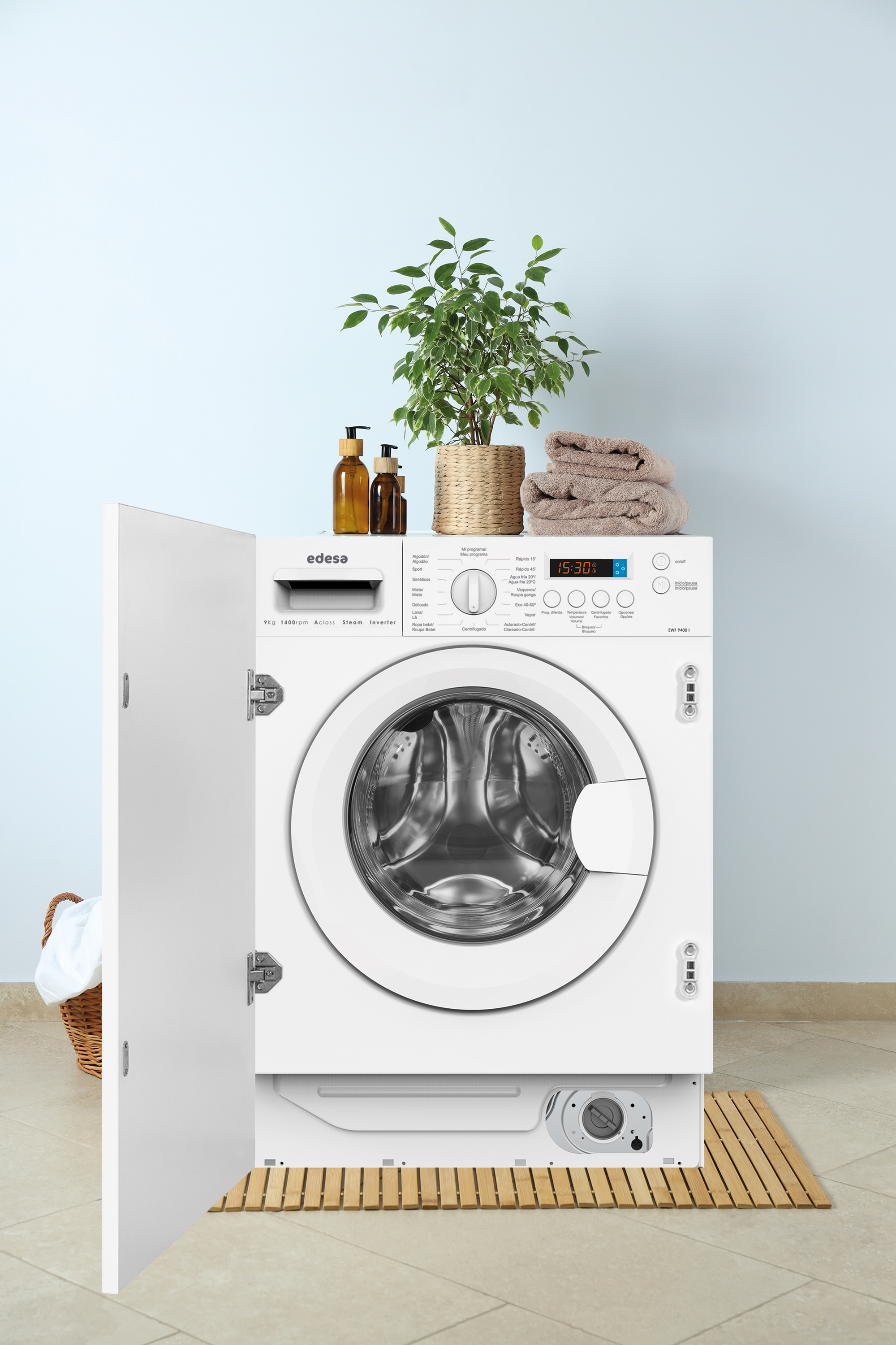 Lavadora blanca con puerta abierta, planta y toallas. Pared azul claro, suelo beige.