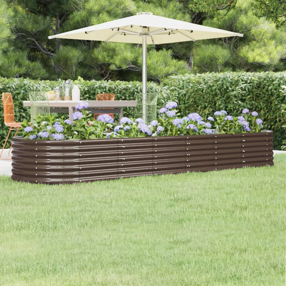 Ein braunes, erhöhtes Gartenbeet mit blauen Blumen. Ein weißer Sonnenschirm und ein Essensemble sind im Hintergrund.