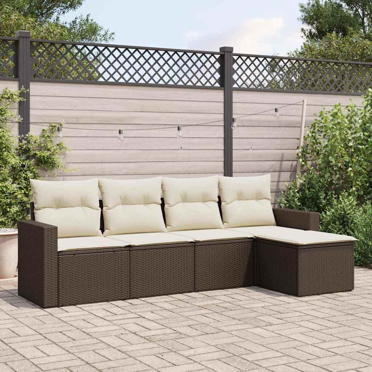 Ein braunes Ecksofa mit cremefarbenen Kissen. Es steht auf einer Steinterrasse mit Zaun und grünen Pflanzen im Hintergrund.