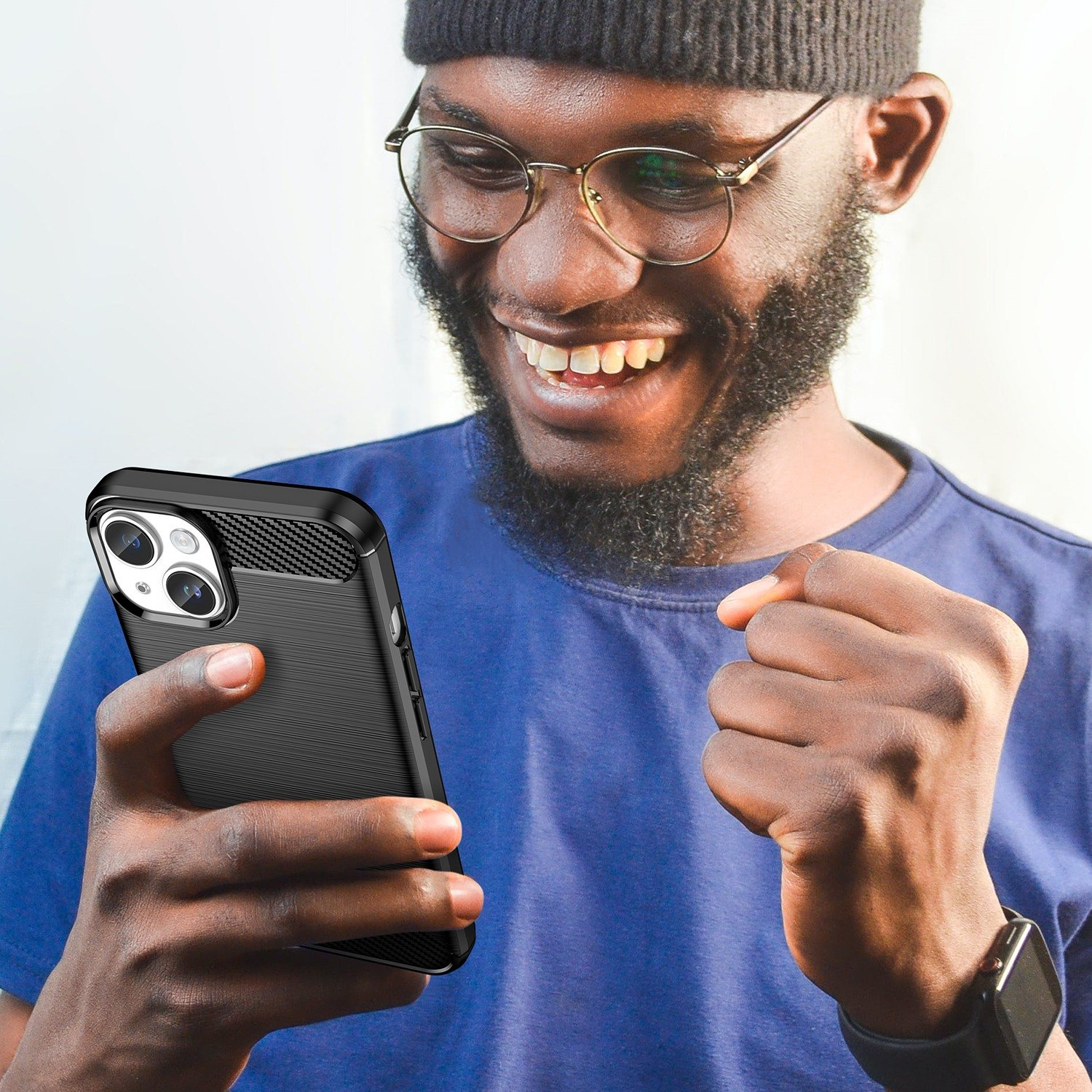 Un hombre negro sonriendo mientras sostiene un teléfono negro con una funda negra. Lleva gafas.