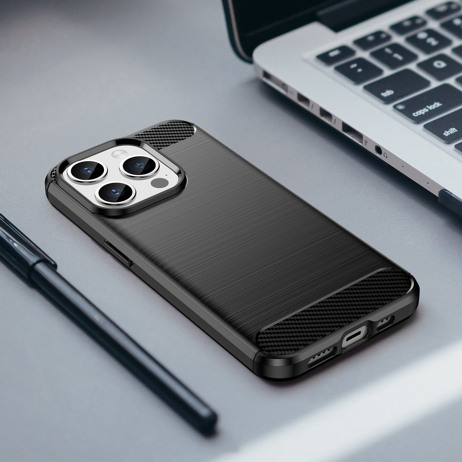Funda negra para teléfono en un escritorio. Un bolígrafo está junto a la funda. Un portátil en el fondo.