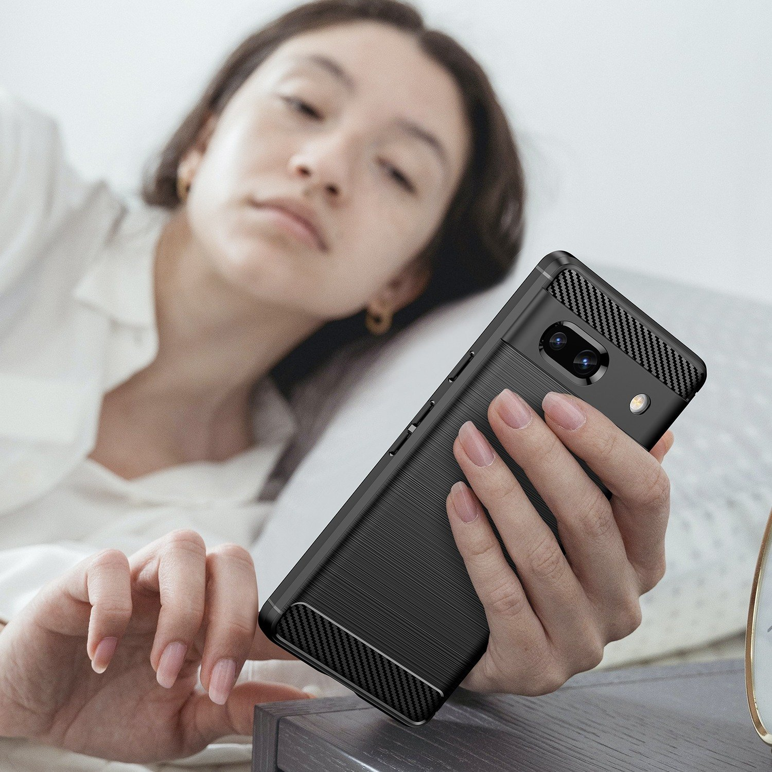 Una persona sosteniendo una funda negra para teléfono, con una cama en el fondo.