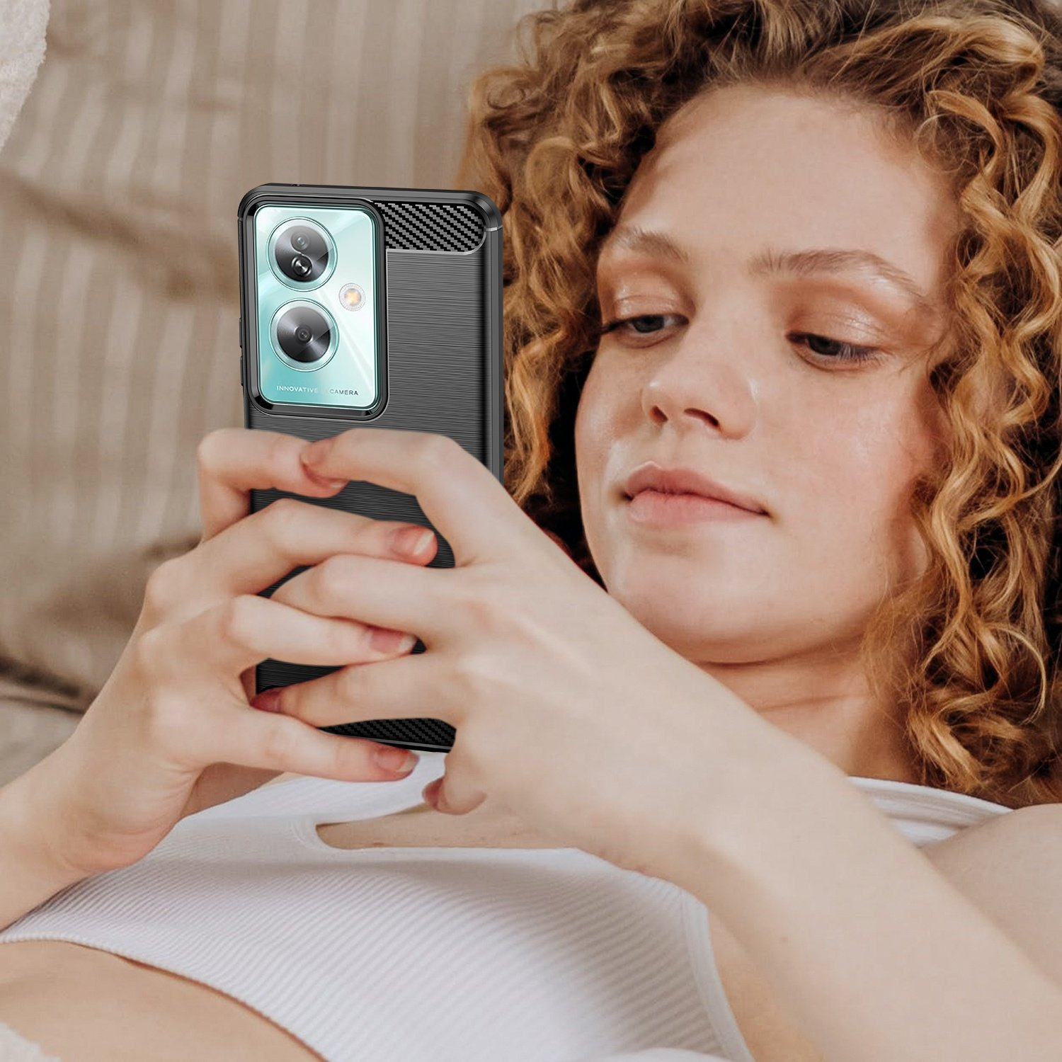 Mujer sosteniendo un teléfono con funda negra. Cabello rizado, mirando abajo.