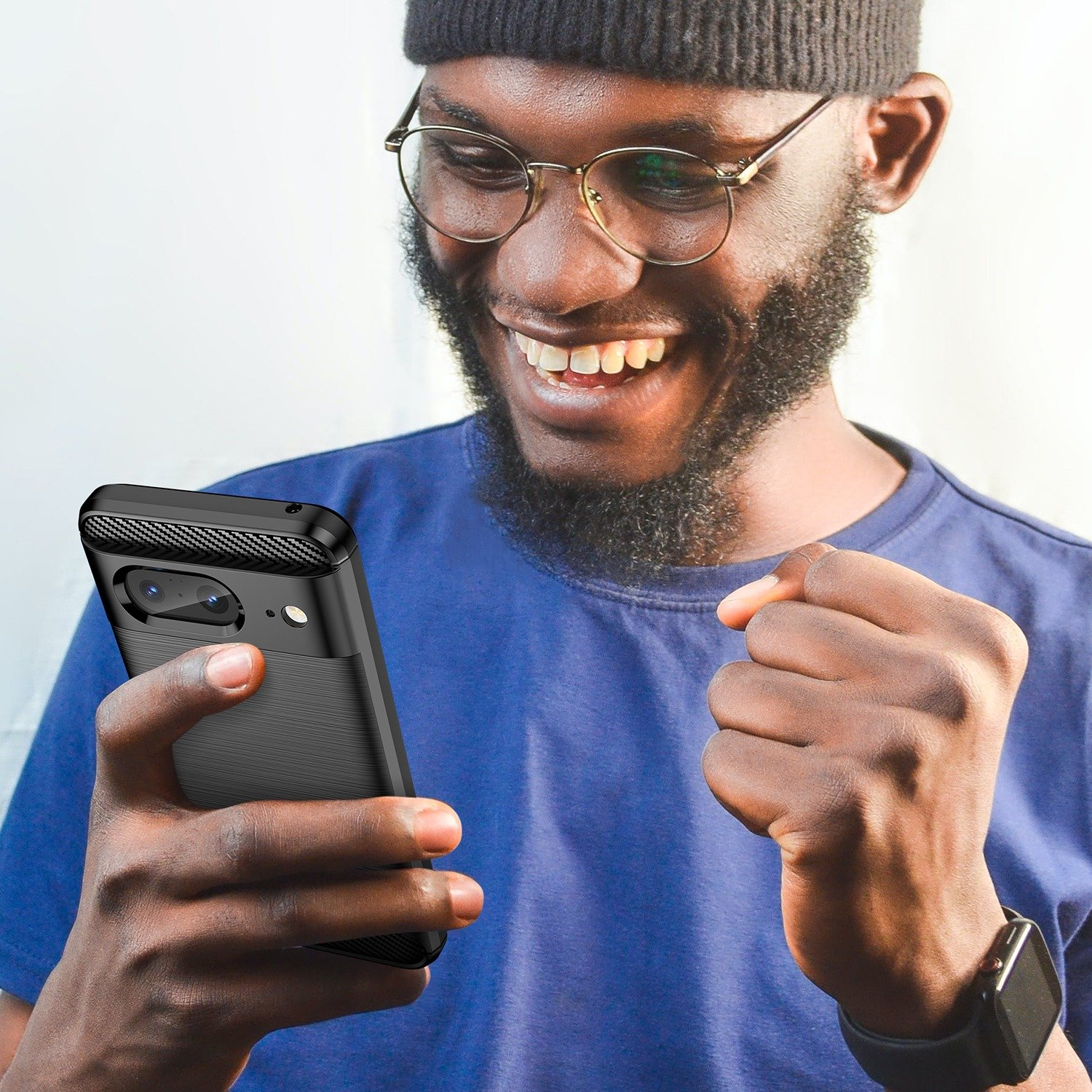 Un hombre sonríe, sosteniendo una funda negra para teléfono. Lleva gafas y una camisa azul.