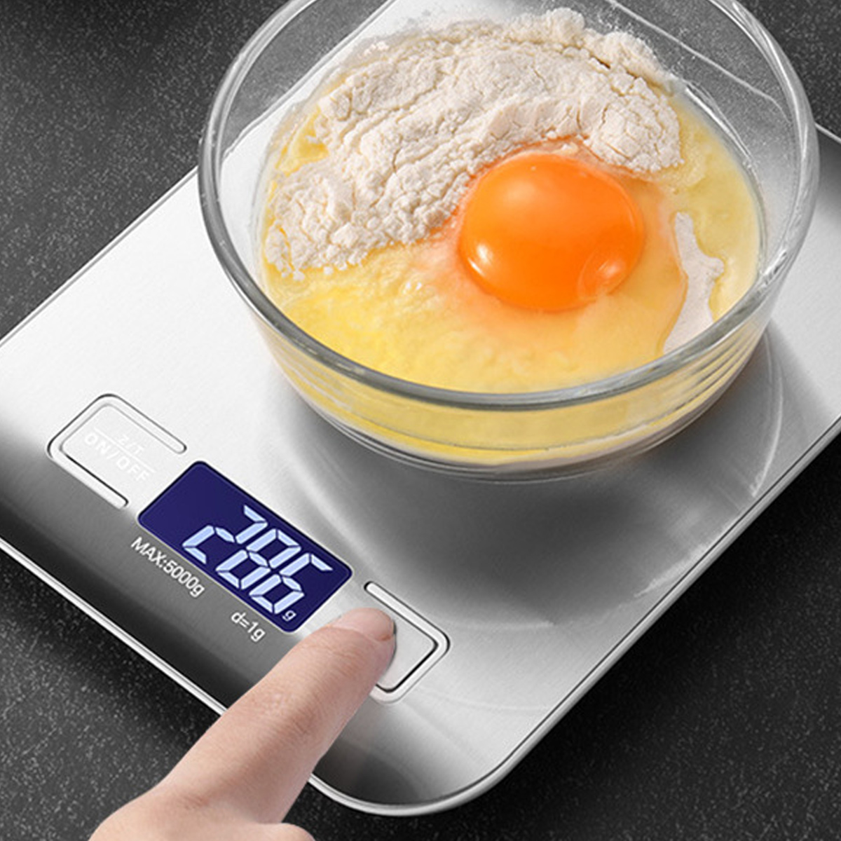 Eine digitale Küchenwaage mit Ei und Mehl in einer Schüssel und einem Finger, der einen Knopf drückt.