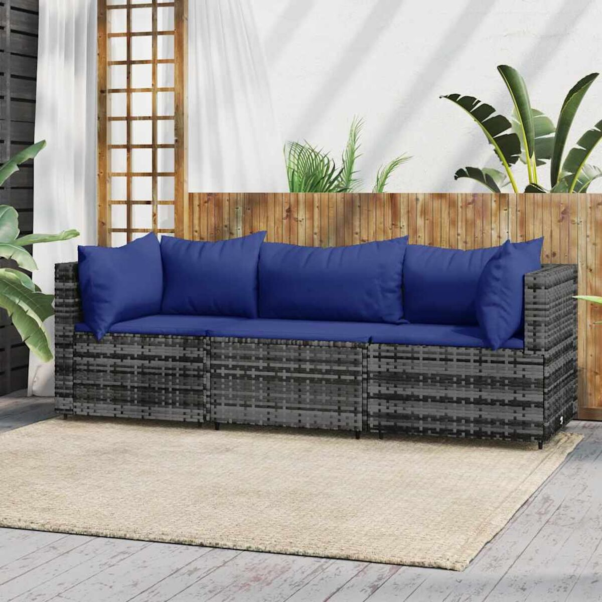 Graues Outdoor-Sofa aus Korbgeflecht mit blauen Kissen, auf Terrasse mit Holzzaun.
