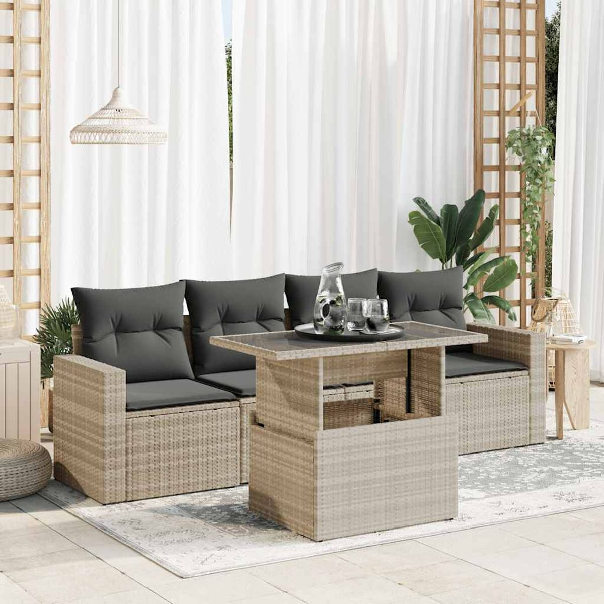 Un sofá seccional exterior con una mesa. Cojines grises, mimbre beige, sobre un patio con cortinas blancas.