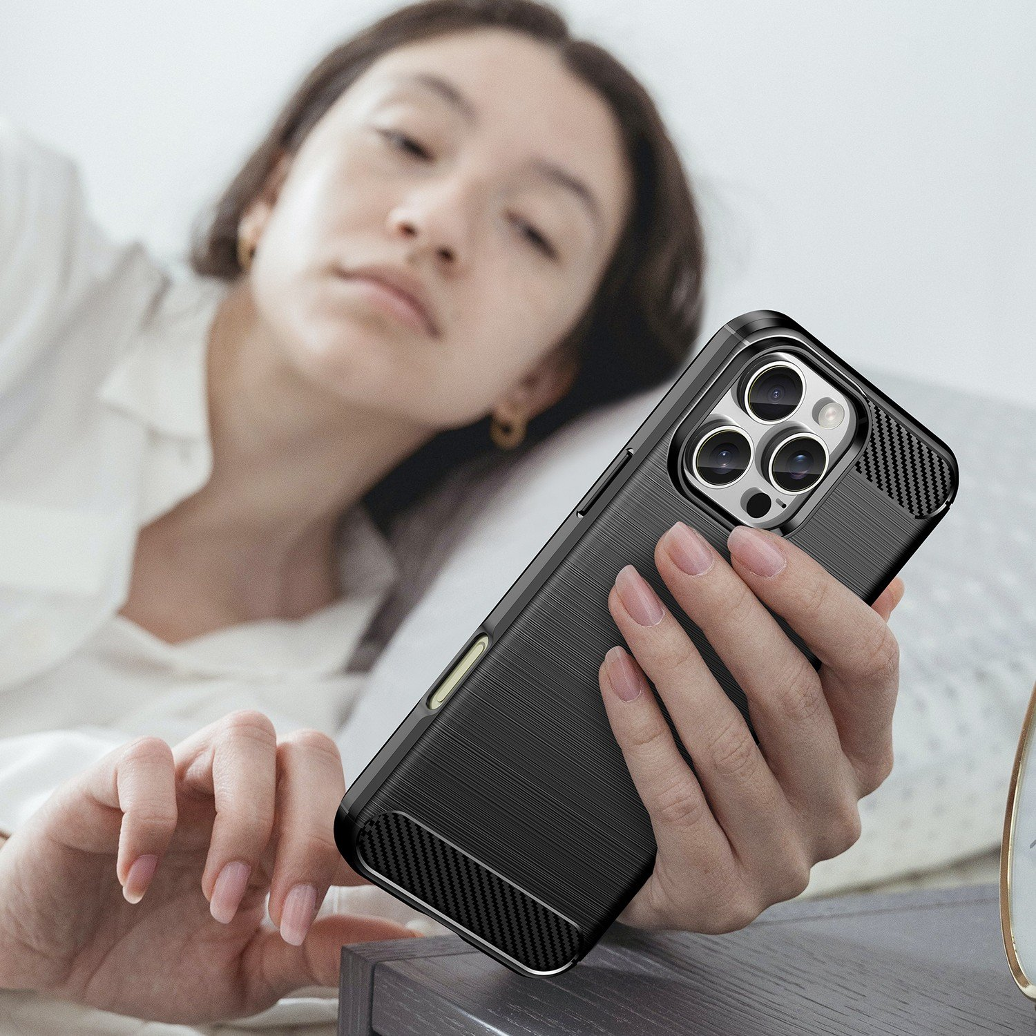 Mujer en la cama sosteniendo un teléfono con una funda negra, mostrando la cámara y los detalles.