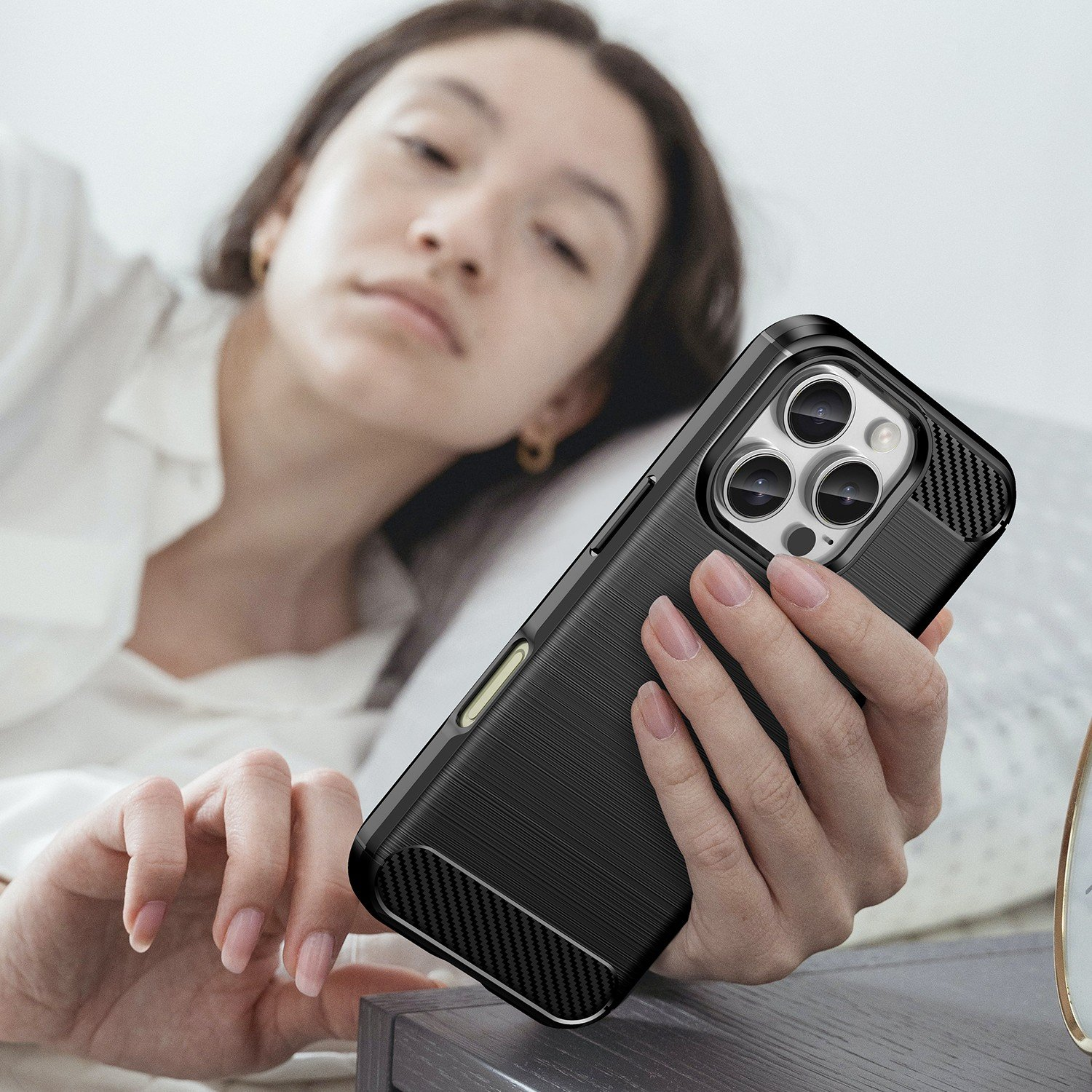 Mujer sosteniendo un teléfono negro con una funda. Está acostada en la cama. La funda es texturizada.