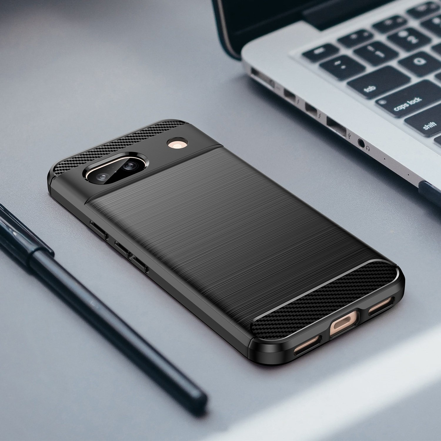 Funda de teléfono negra junto a un bolígrafo sobre un escritorio gris. Fondo blanco.