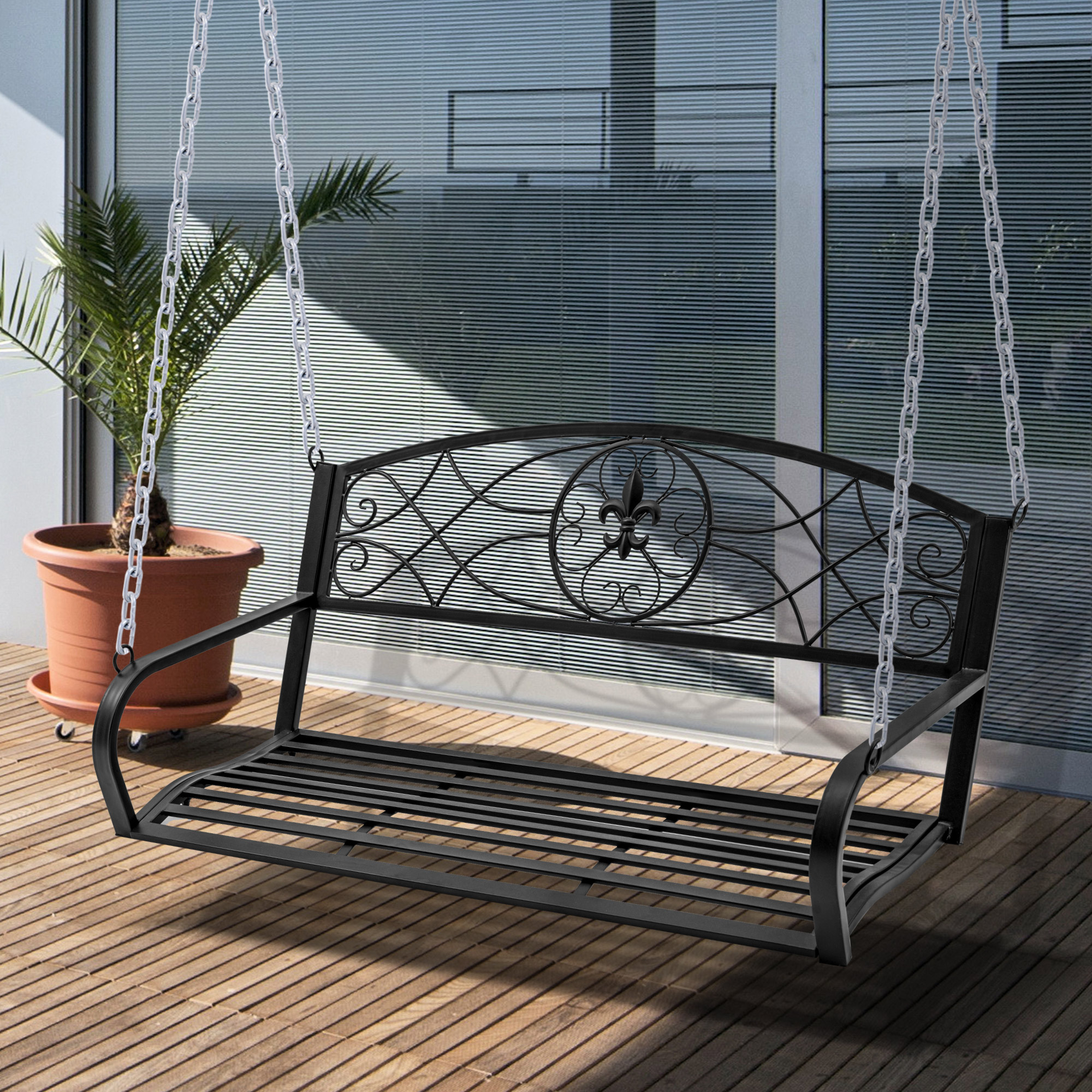Schwarze Metallschaukel, die an Ketten hängt. Eine Topfpalme steht im Hintergrund auf einem Holzdeck.