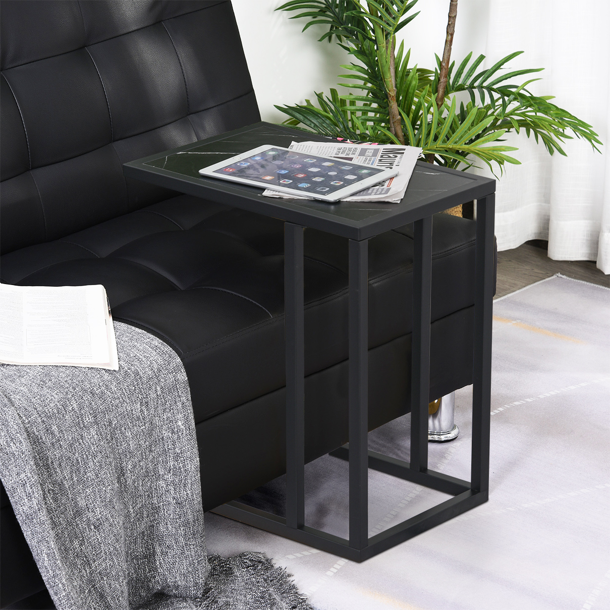 Ein schwarzer Beistelltisch neben einem schwarzen Ledersofa mit Tablet und Zeitung darauf.