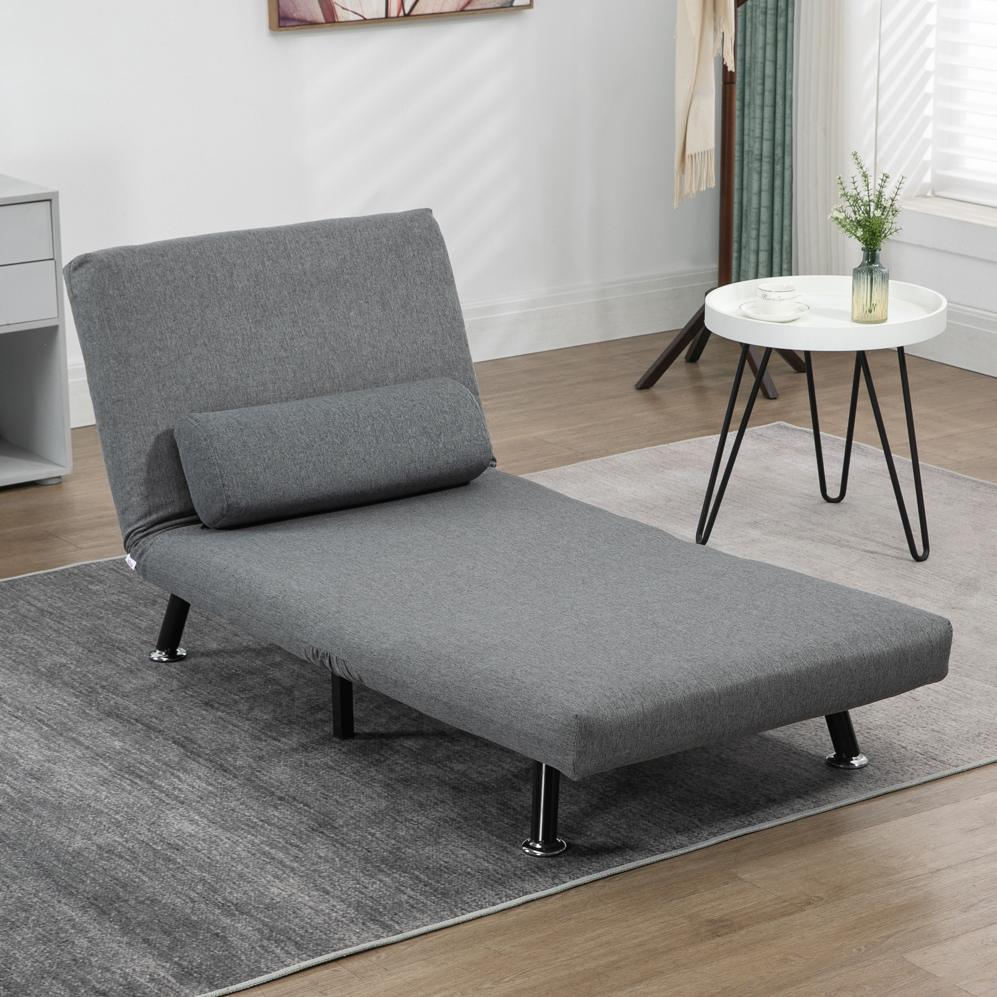 Graue Chaiselongue mit Kissen auf grauem Teppich, neben einem Tisch.