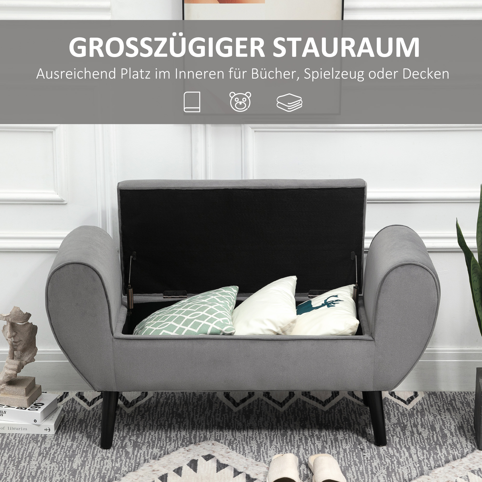 Eine graue Aufbewahrungsbank mit offenem Deckel, die Kissen und Bücher im Inneren zeigt.