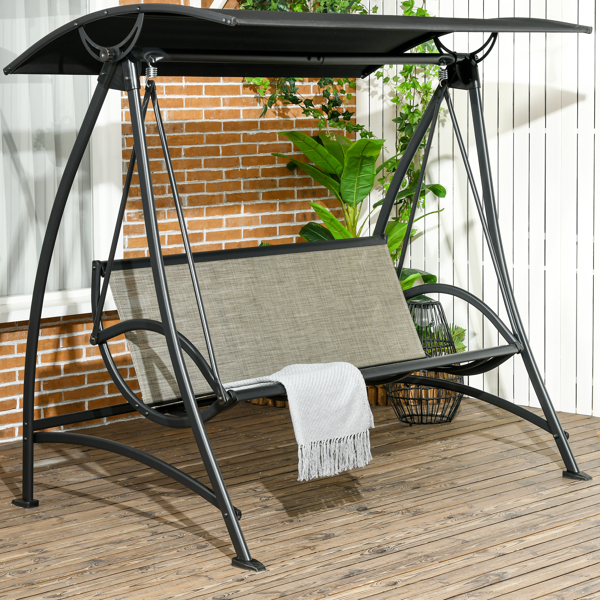 Schwarze Schaukel mit grauem Sitz, schwarzem Baldachin und Holzterrasse im Vordergrund.