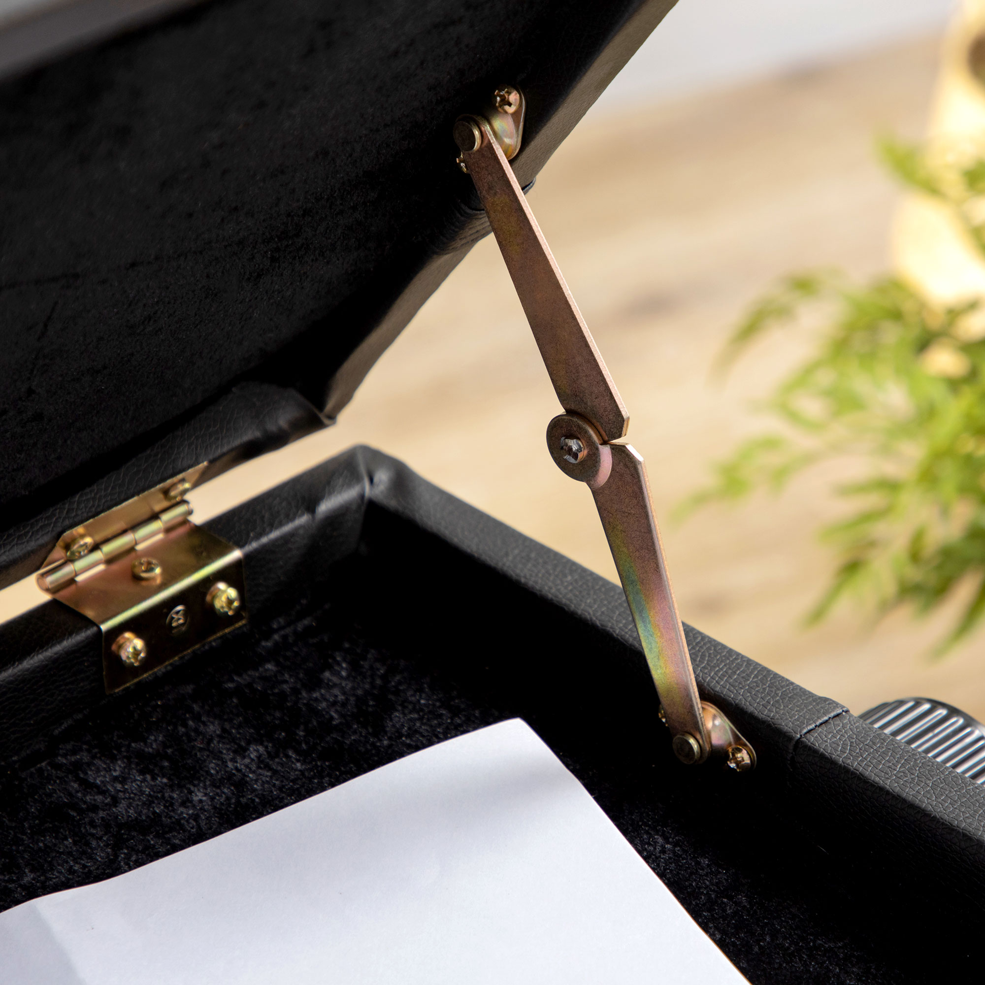 Geöffnete schwarze Aufbewahrungsbox mit Metallscharnier und einem Papierstück darin.