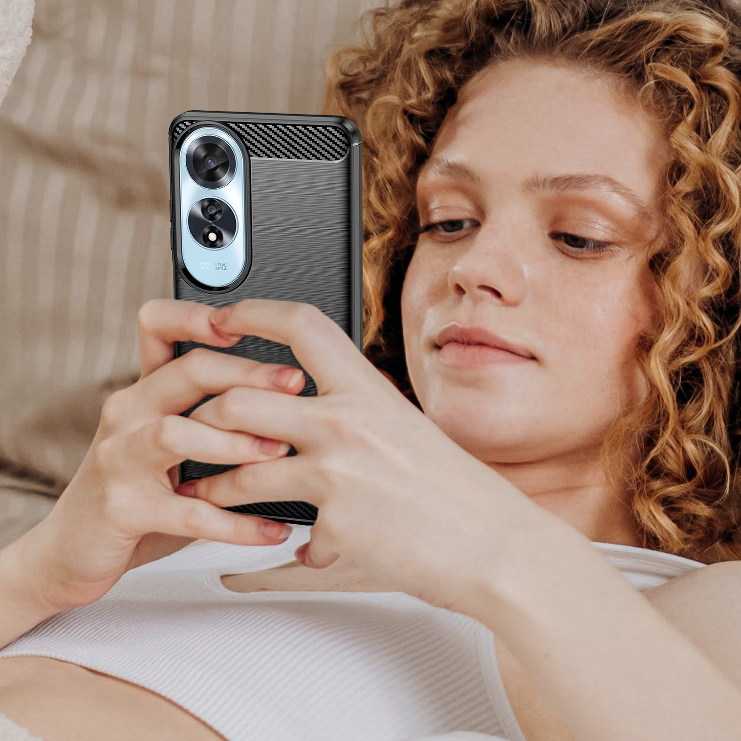 Una mujer con cabello rizado sosteniendo un teléfono en una funda negra, mirando la pantalla.