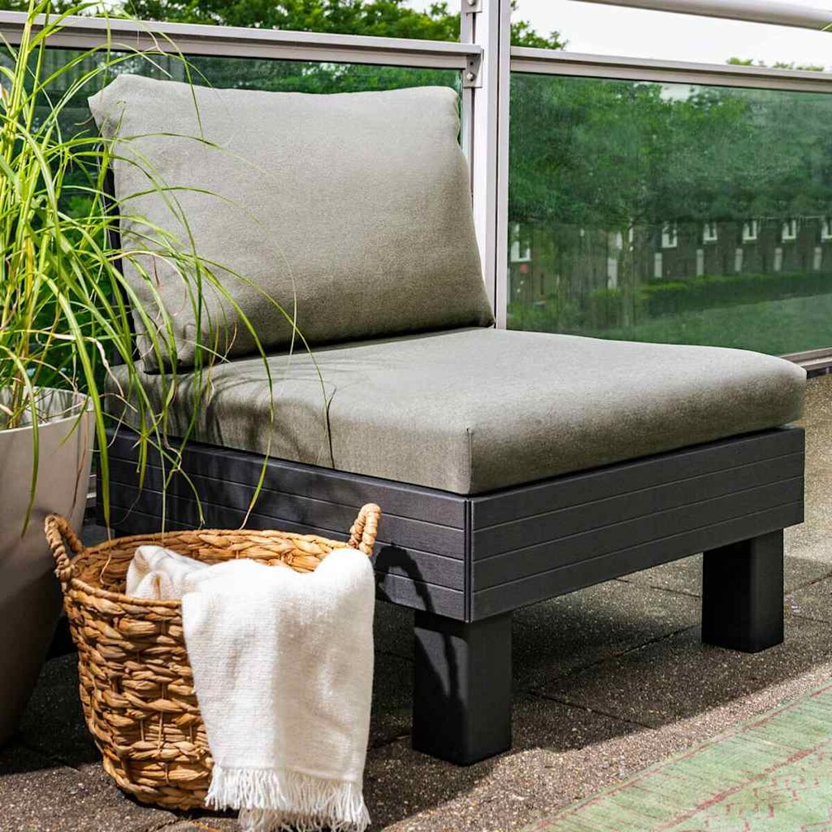 Outdoor-Sitzgruppe mit grauem Kissen, Korb und weißer Decke.