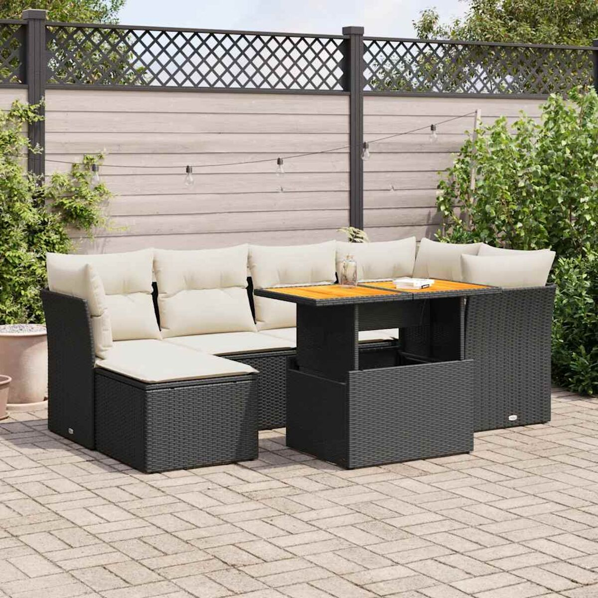 Set di mobili da patio: divano, tavolo con piano sollevabile e sfondo di piante e recinzione.