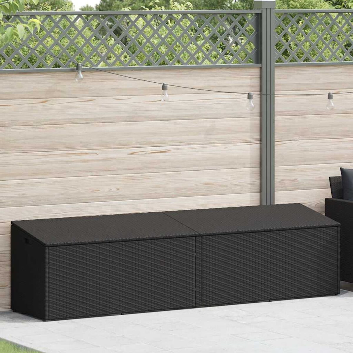 Schwarze Outdoor-Aufbewahrungsbank mit zwei Abschnitten, platziert vor einem Holzzaun und einem Gitterzaun.