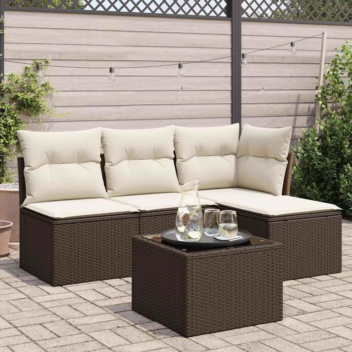 Set di divani in vimini marrone per esterni con cuscini beige e tavolo in vetro.