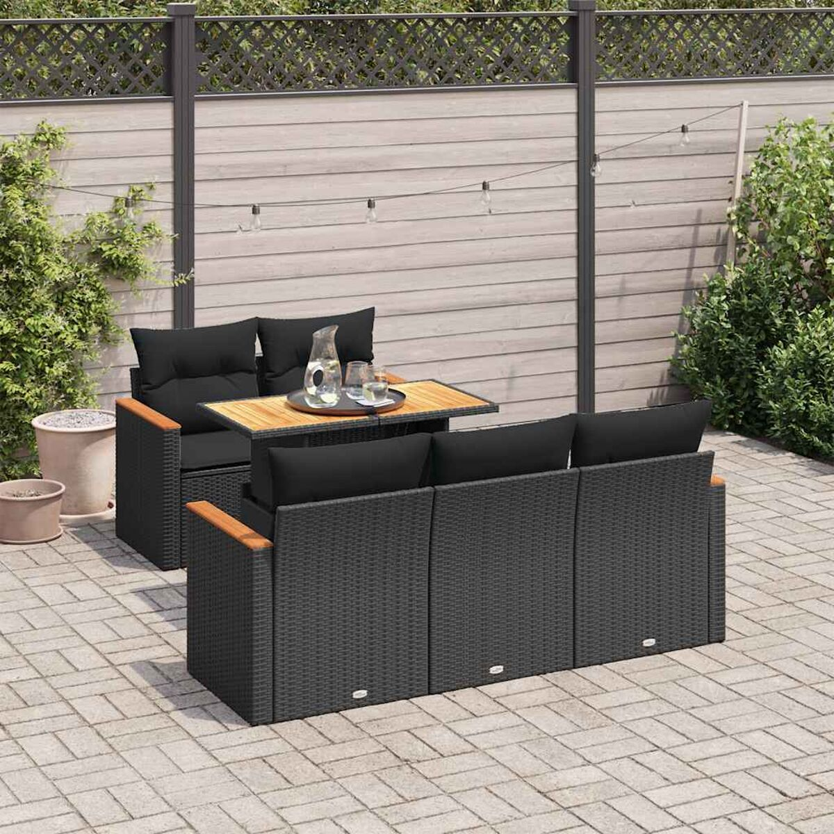 Un set di divani in rattan nero con cuscini neri e un tavolo in legno. Si trova su un patio in mattoni.