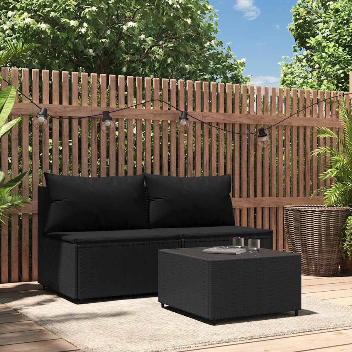 Schwarzes Outdoor-Sitzset. Enthält Sofa, Tisch und Kissen. Holzzaun.