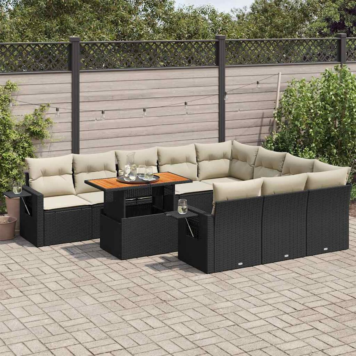 Set da patio esterno con vimini nero, cuscini beige, un tavolo in legno e bicchieri sul tavolo.