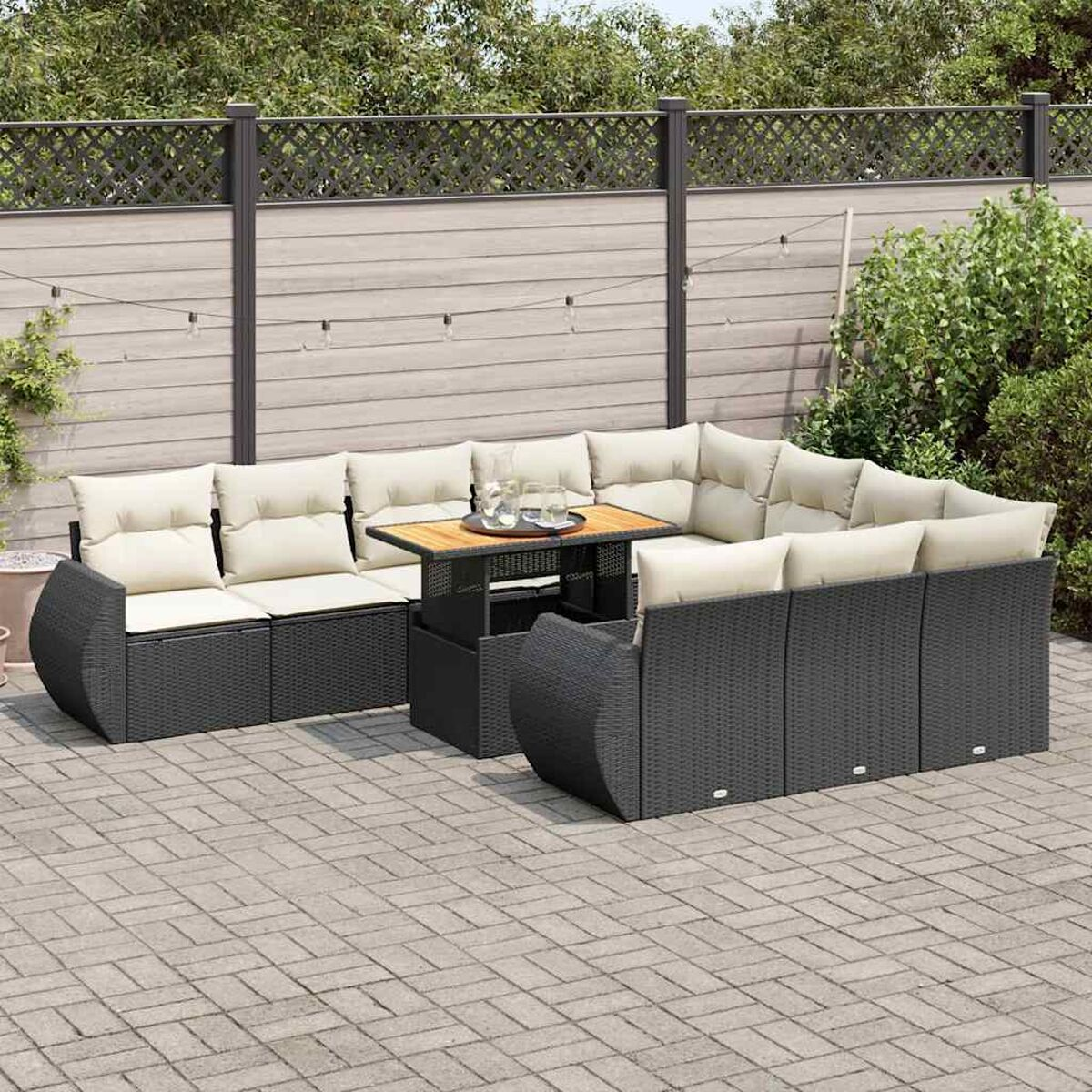 Un set di mobili da esterno in vimini nero disposto su un patio in mattoni, con un tavolo di legno.