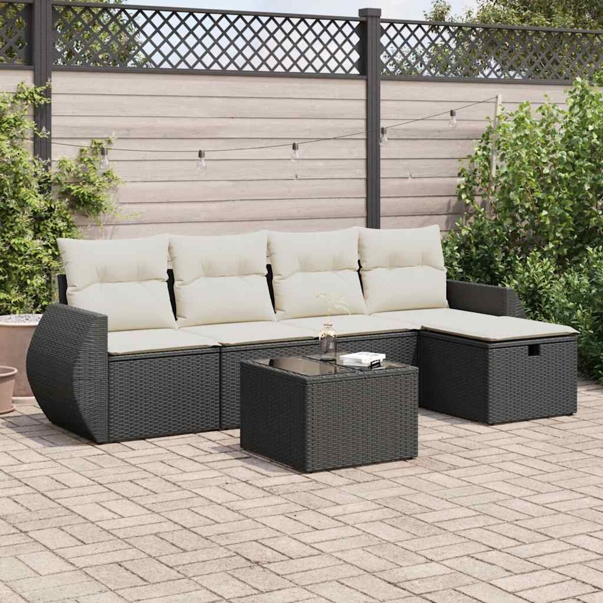 Schwarzes Outdoor-Wicker-Möbelset mit cremefarbenen Kissen, Tisch und Chaiselongue auf einer Terrasse. Weißer Hintergrund.