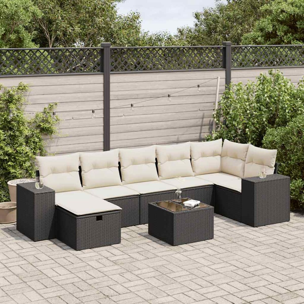 Eine dunkle Sitzgruppe für den Außenbereich mit beigen Kissen. Sie steht auf einer Backstein-Terrasse mit Pflanzen.