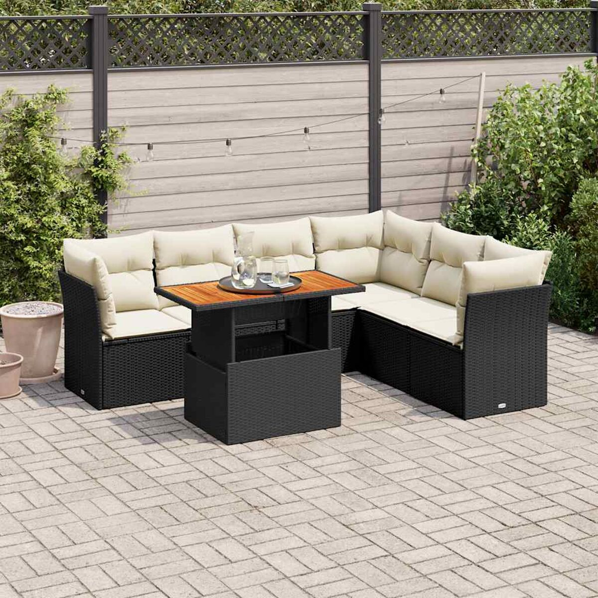 Un set da patio all'aperto con un divano componibile in vimini nero, tavolo in legno e accessori, e piante.
