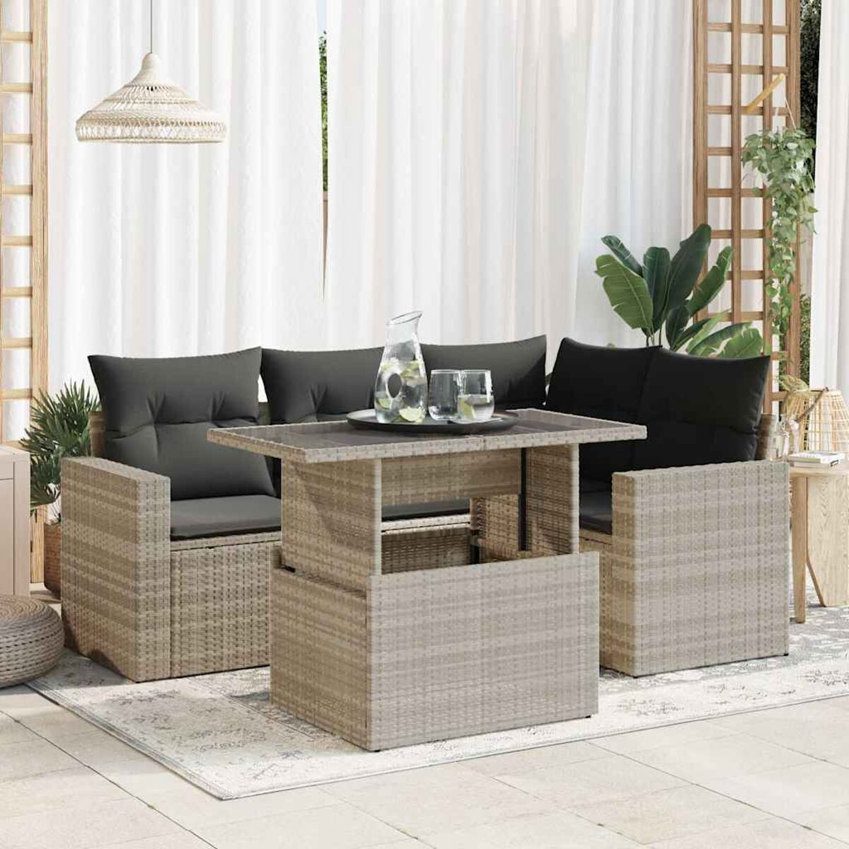 Set divani in vimini da esterno con tavolo rialzabile. Lo sfondo include tende e piante.
