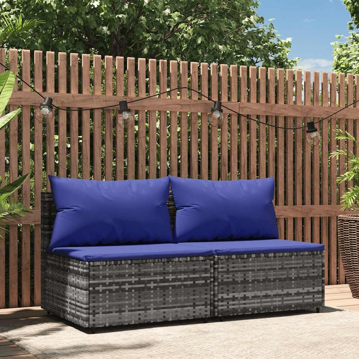 Ein Outdoor-Sofa mit blauen Kissen auf einem Holzdeck mit Lichterketten.