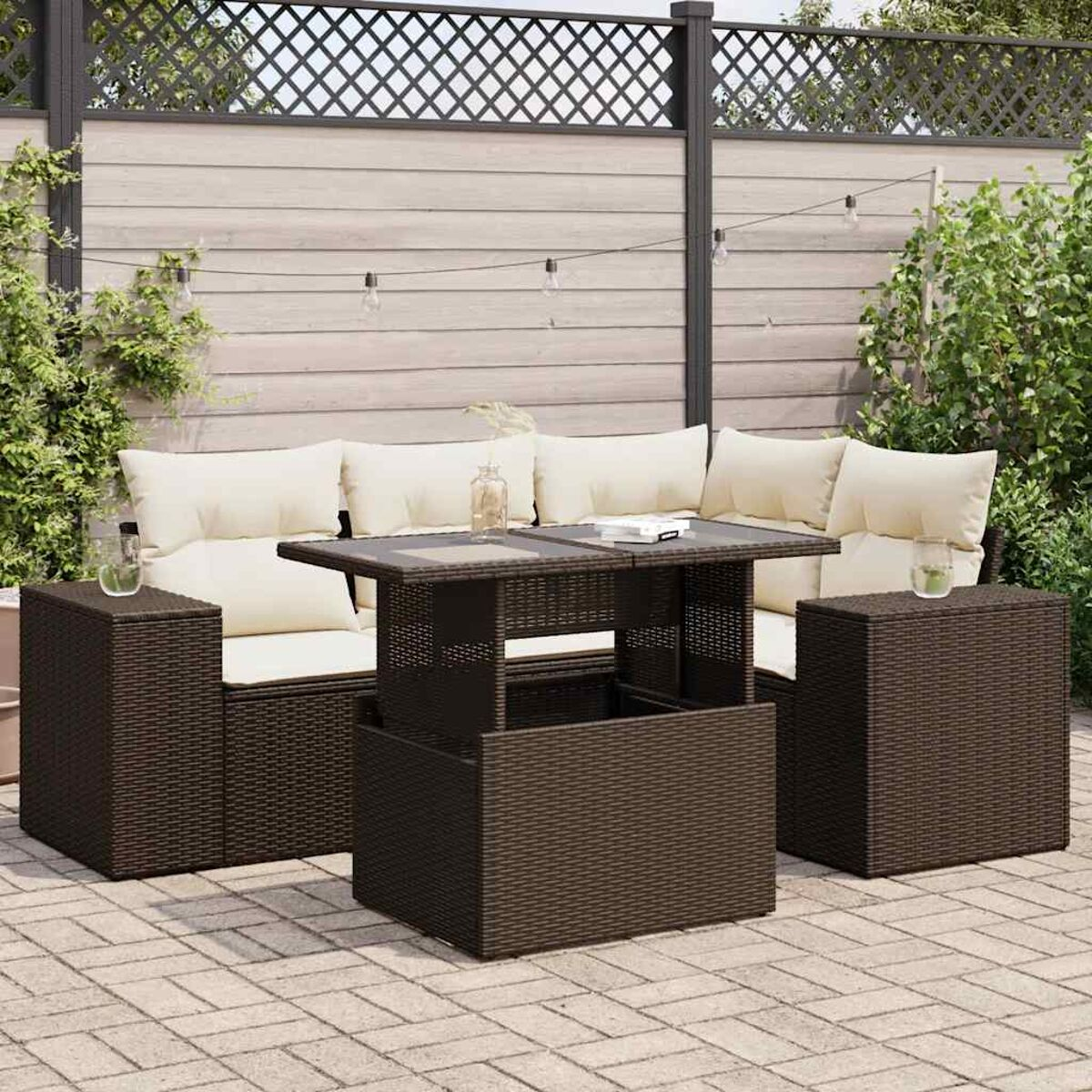 Set da patio esterno con mobili in vimini marroni, cuscini color crema e tavolo con piano in vetro.
