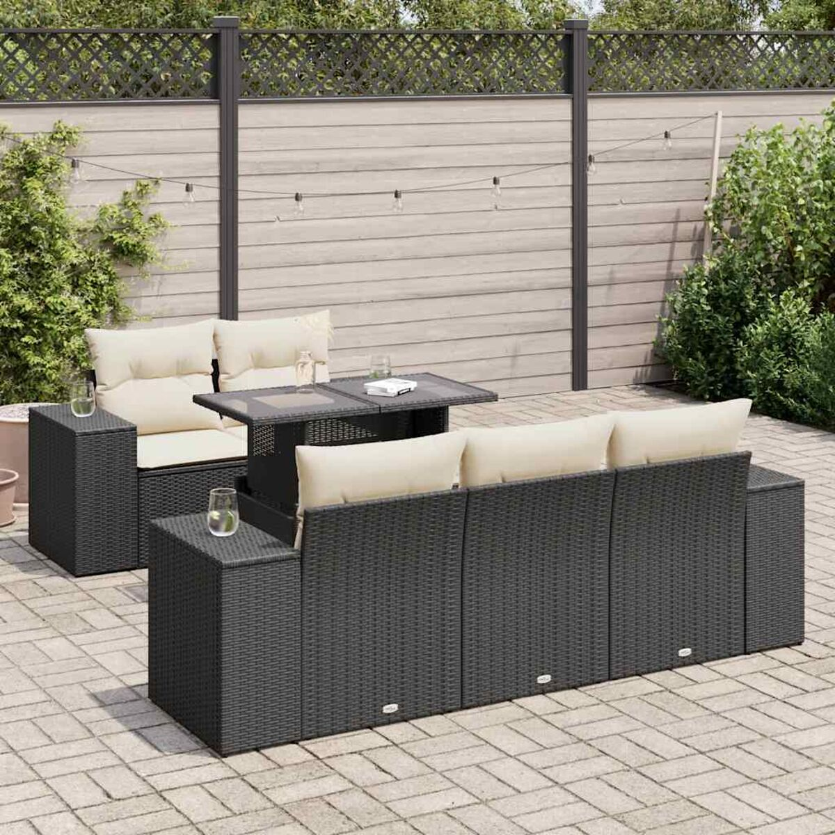 Schwarzes Outdoor-Korbsessel-Set mit beigen Kissen. Ziegel-Patio, Holzzaun mit Lichtern.