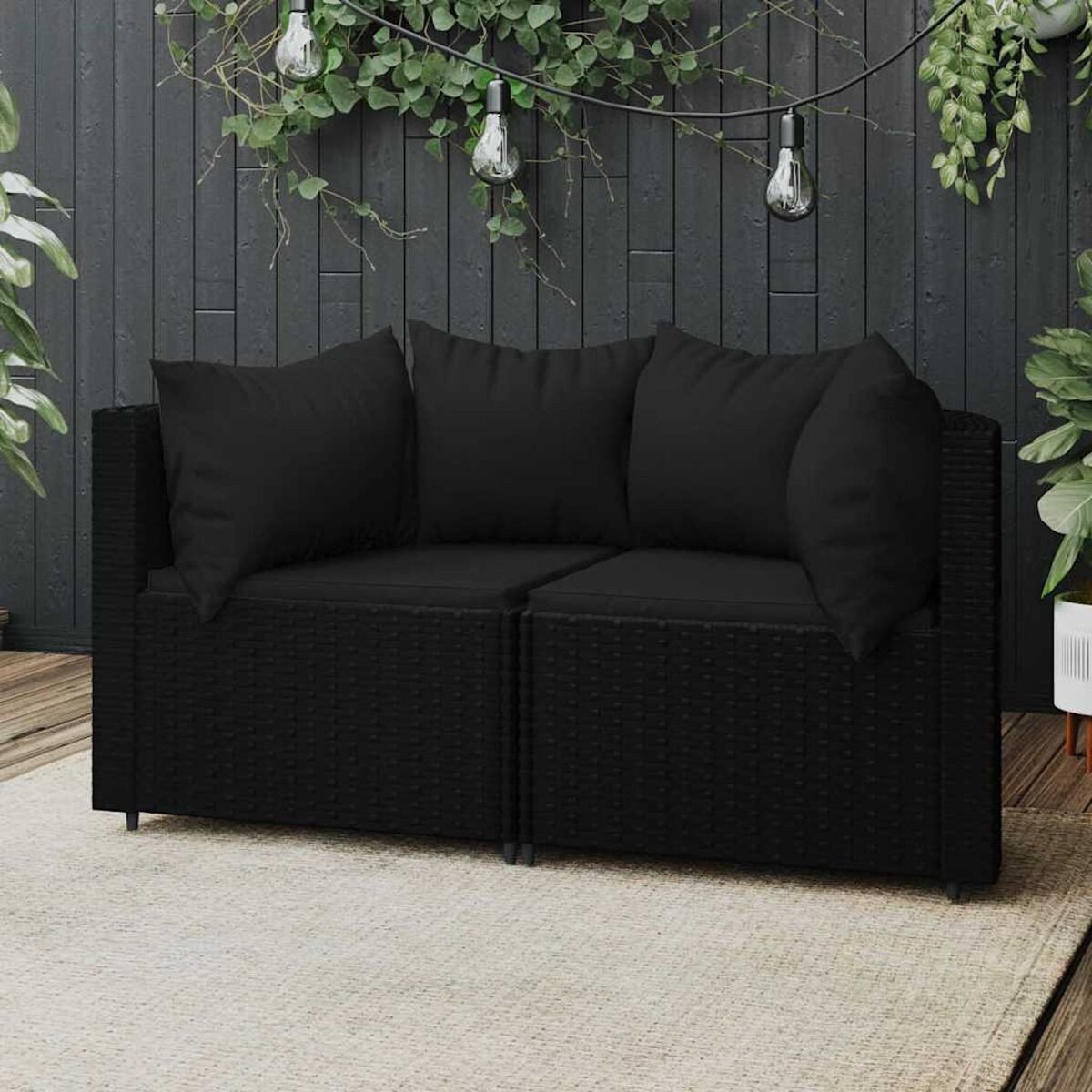 Zwei schwarz gepolsterte Rattan-Sofas auf einem neutralen Teppich, Pflanzen im Hintergrund.