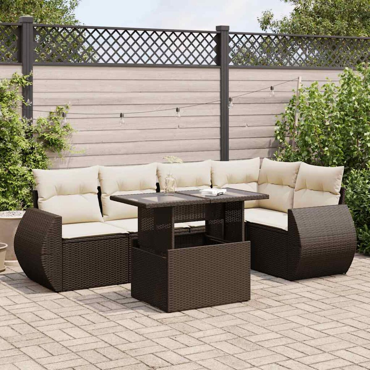 Braunes Outdoor-Sofa aus Korbgeflecht mit beigen Kissen und einem braunen Tisch. Im Hintergrund ist ein Zaun.