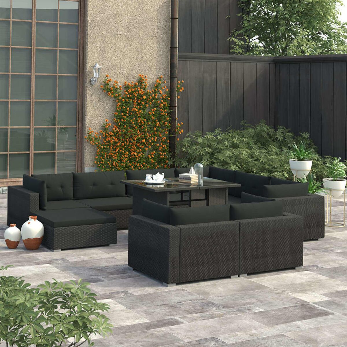 Terrassenmöbel-Set mit schwarzen Rattanmöbeln und einem Glastisch auf einer Steinterrasse.