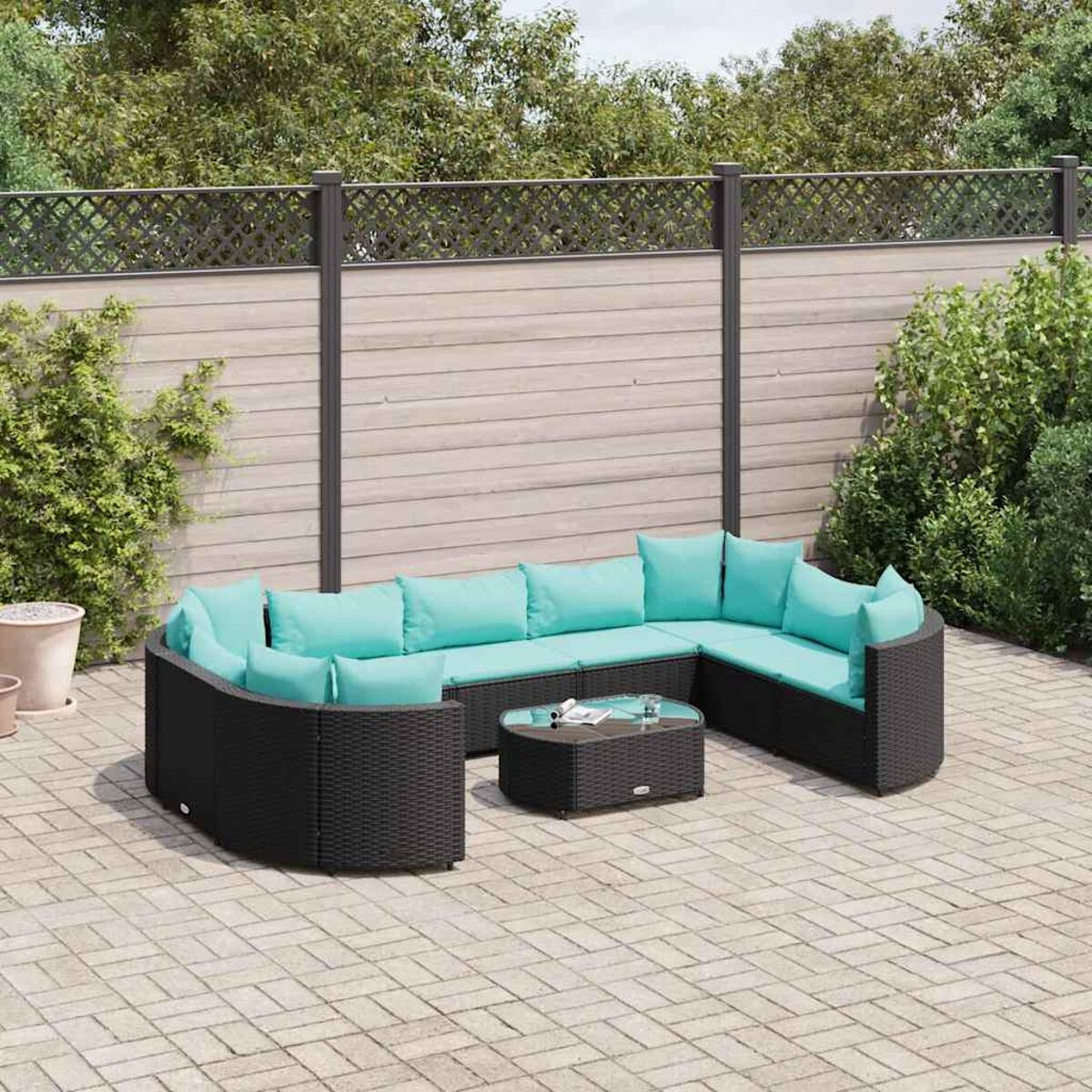 Un divano angolare nero per esterni con cuscini verde acqua, un tavolo abbinato e un patio in mattoni in un giardino.