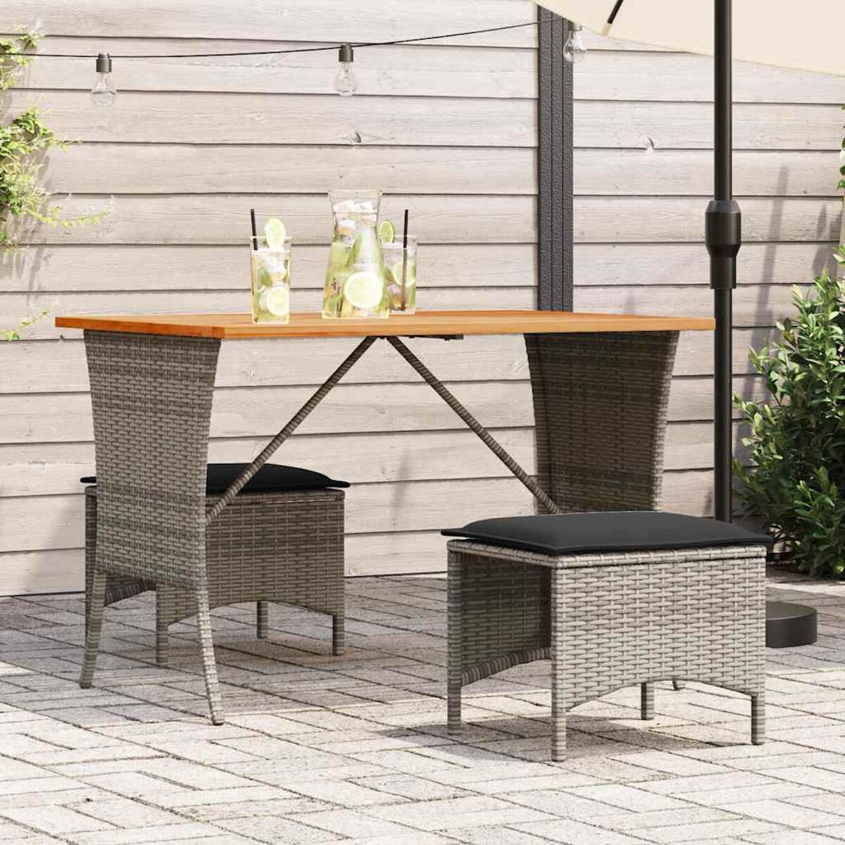 Set da pranzo all'aperto con tavolo in legno, due sedie e due sgabelli su un patio in pietra.