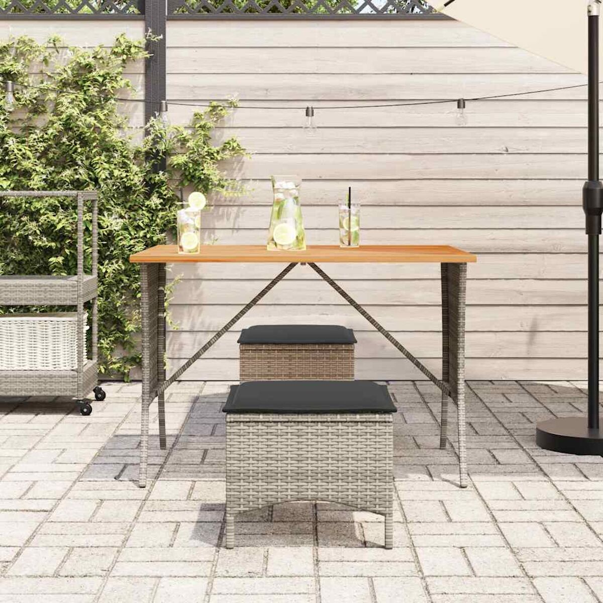 Un set da patio con un tavolo in legno, due sgabelli e uno sfondo di giardino.